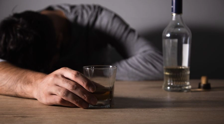 Man passed out on table with hand of glass of alcohol and bottle nearby displaying Bipolar Disorder and Alcoholism