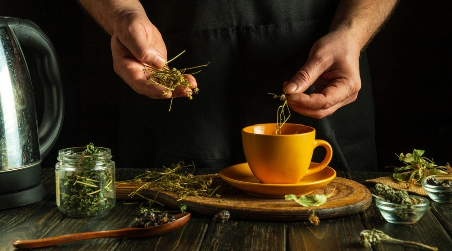 Two hands putting herbs in tea cup with assorted herbs on table - Cocaine Detox Myths - Drinking Herbal Combinations