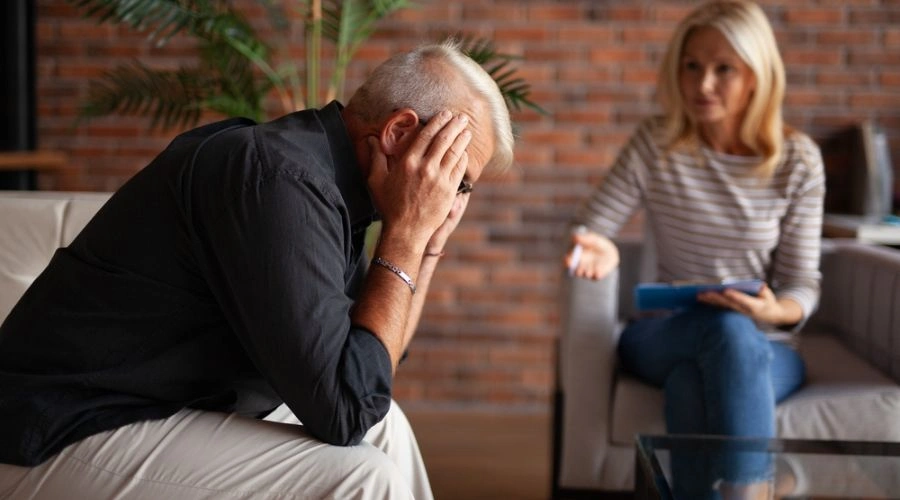 Man holding his hands on his face next to a counselor displaying Dual Diagnosis of PTSD