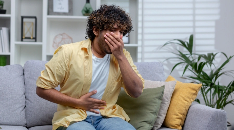Man sitting on sofa yawning and displaying the Potential Adverse Reactions of Naltrexone