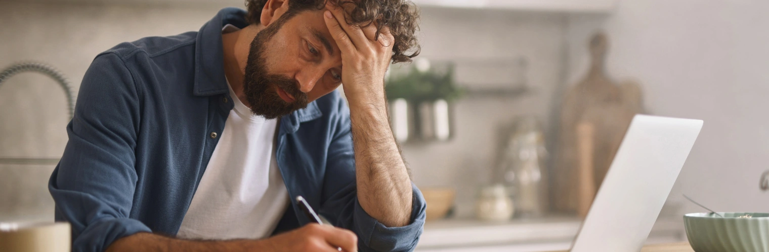 Image of a man sitting at a desk writing with one hand and other hand on his head - AA Fear Inventory Examples And Worksheet - Icarus Nevada