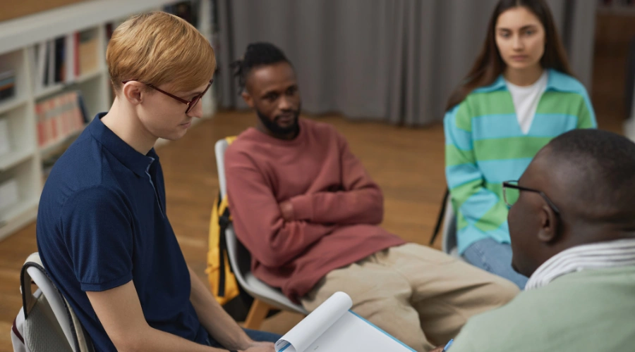 Image of a man reading in therapy, surrounded by his counselor, along with a man and woman alos in treatment - Different treatment paths for alcohol addiction recovery at Icarus Nevada