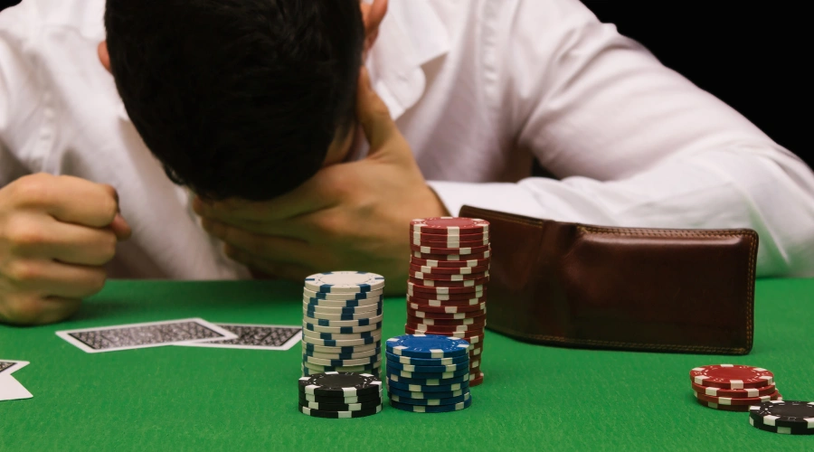 Image of a male gambler in anguish in a casino with his head on a craps table beside three rows of chips.