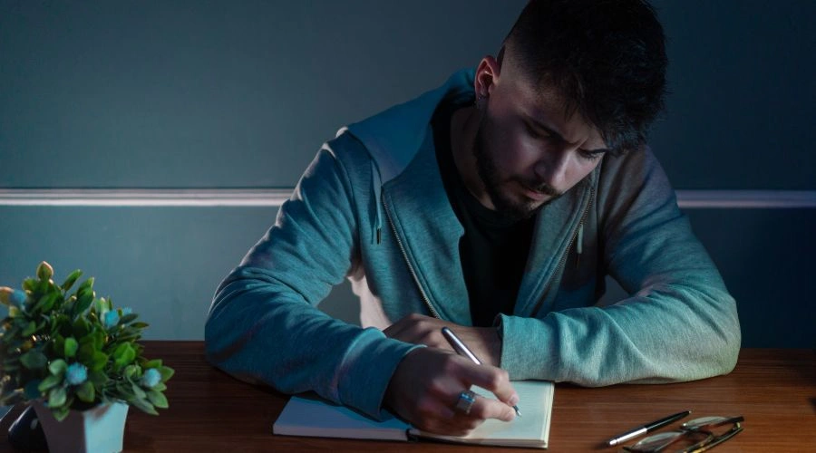 Person writing in a journal, recalling past unacceptable behaviors linked to alcohol use