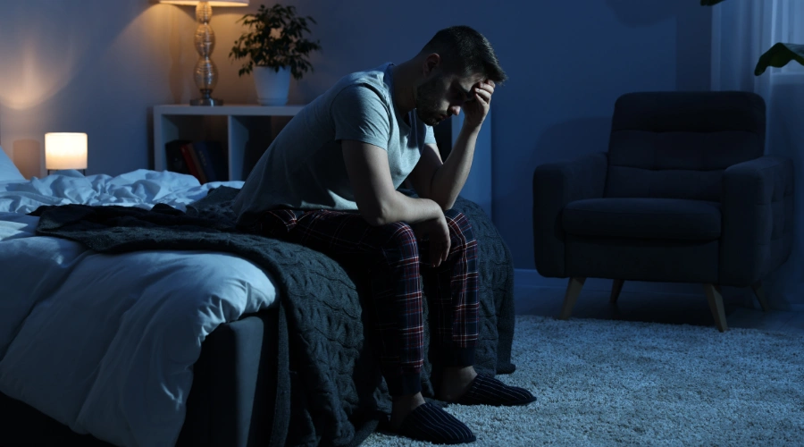 Image of a frustrated man sitting on bed holding his hand on his head