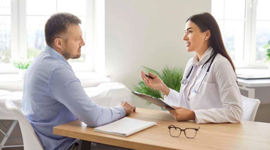 Image of a male patient sitting at a table and listening to a female physician