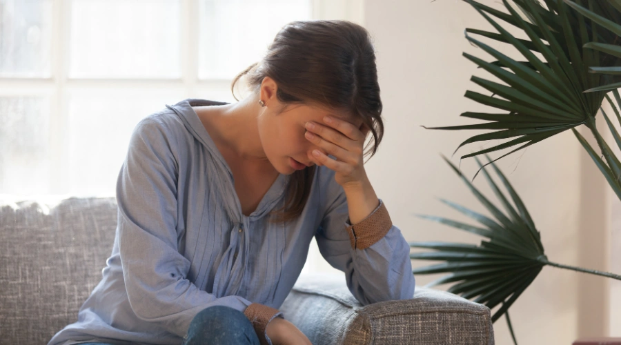 Image of woman sitting on a sofa with one hand covering her face, experiencing an emotional meltdown and showing signs of stress
