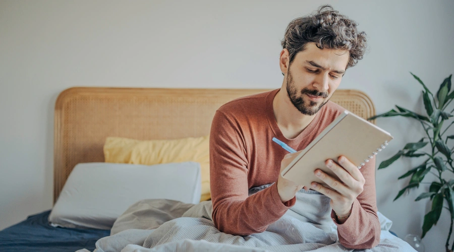 Image of a man sitting in bed writing a Moral Inventory for AA Purposes