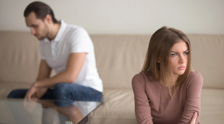 Image of a woman and man sitting apart on a sofa displaying the strained relationship between loved ones affected by trauma