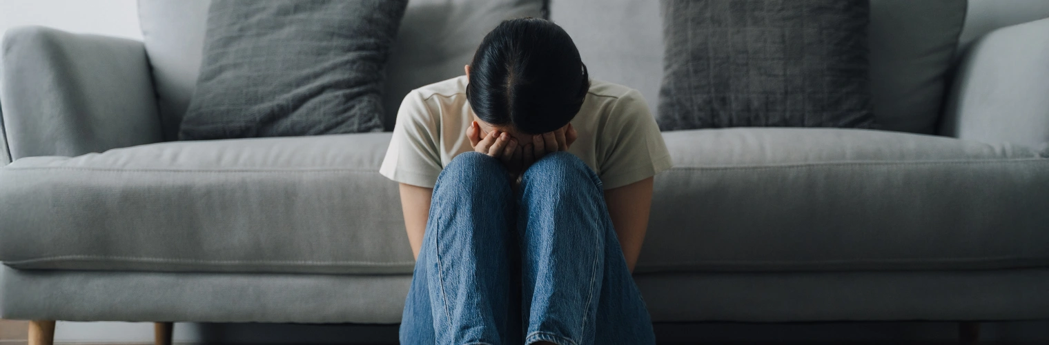 Image of a female sitting in front of a sofa with her face of her knees and both hands covering her face - What Is A Trauma Meltdown - Icarus Behavioral Health Nevada