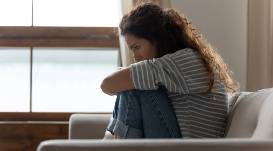 Image of a young lady sitting on a sofa, grasping her knees