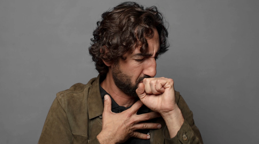 Image of a man coughing while holding a joint, showing the health effects of long-term marijuana use