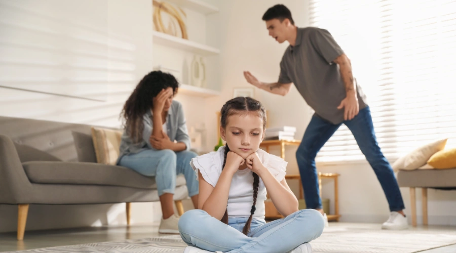 Image of a young girl sitting on the floor in front of her parents arguing in the background