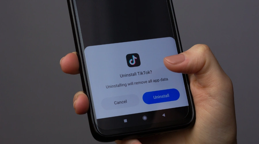 Image of a woman holding a smartphone and uninstalling the TikTok app