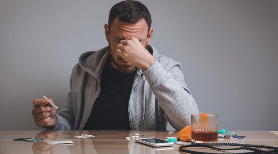 Image of a man sitting alone at a table with drug paraphernalia, looking distressed, symbolizing the dangers and high overdose risk of fish scale cocaine use