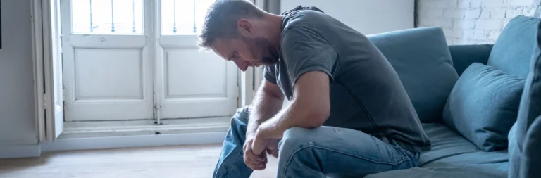 Image of a man sitting on a sofa in deep pain and anguish - What are the Signs Someone Is on Meth - Icarus Behavioral Health Nevada