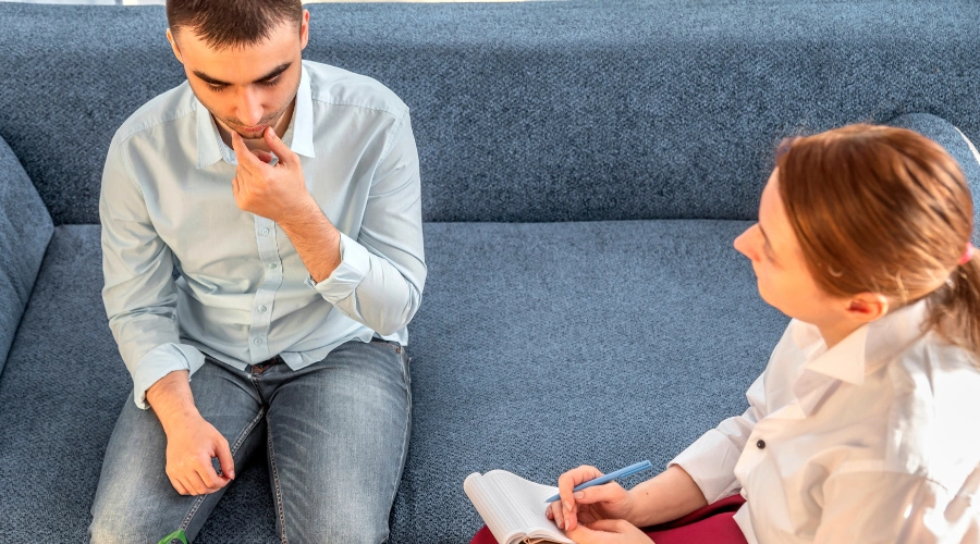 Image of a man sitting on a sofa participating in a personalized rehab therapy session with a counselor at Icarus Las Vegas