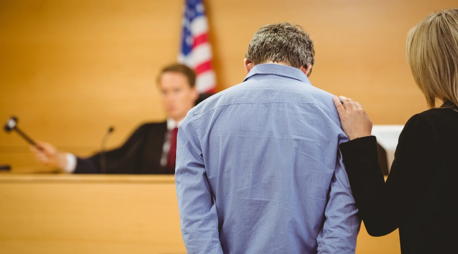 Image of a man standing with his counselor in front of a Judge, who is approving court-ordered rehab as an alternative to jail