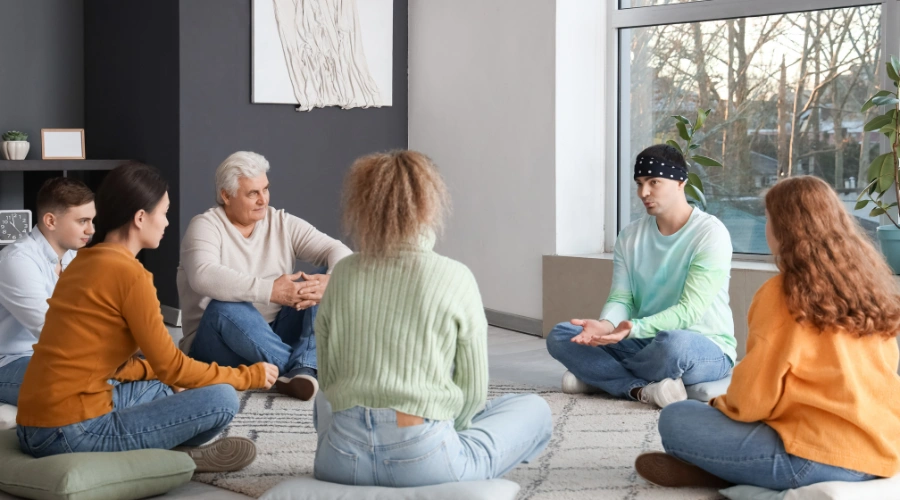 Image of men and women sitting in an AA support group meeting circle, displaying their belief and acceptance of help in AA recovery
