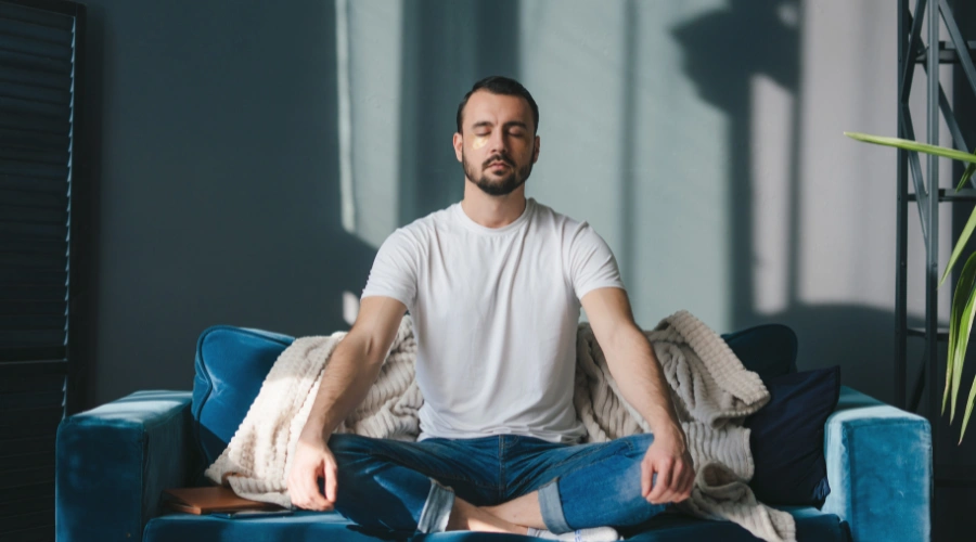 Image of a man sitting in a yoga position on the floor and meditating, displaying hope and open-mindedness gained through AA Step 2