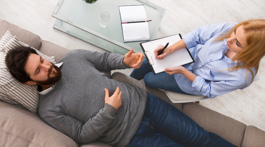 Image of a man laying down on a sofa during residential mental health treatment at Icarus Nevada as a therapist looks on, writing down information